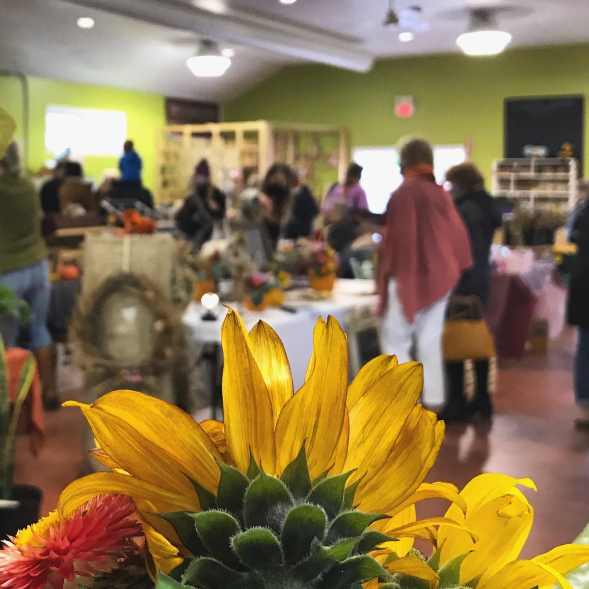 A bright green room with vendors' tables and flowers in the foreground