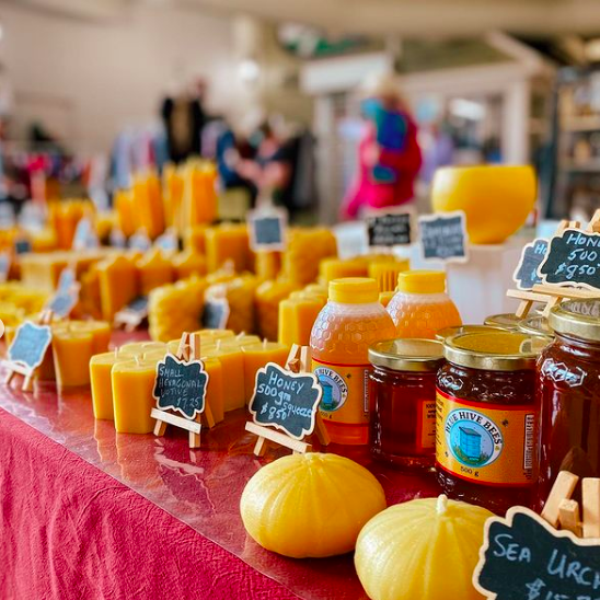 A table displaying beeswax and honey products in the foreground, with other vendor tables in the background