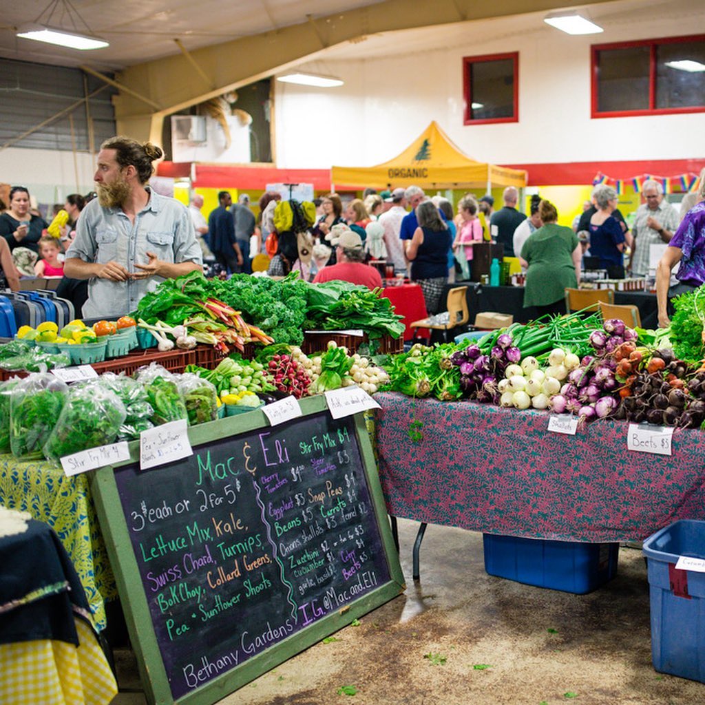 A large room filled with vendors' tables, with a produce stall and its vendor in the foreground