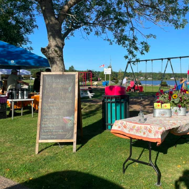 A table and chalkboard welcome visitors to the market in a grassy, oceanside park